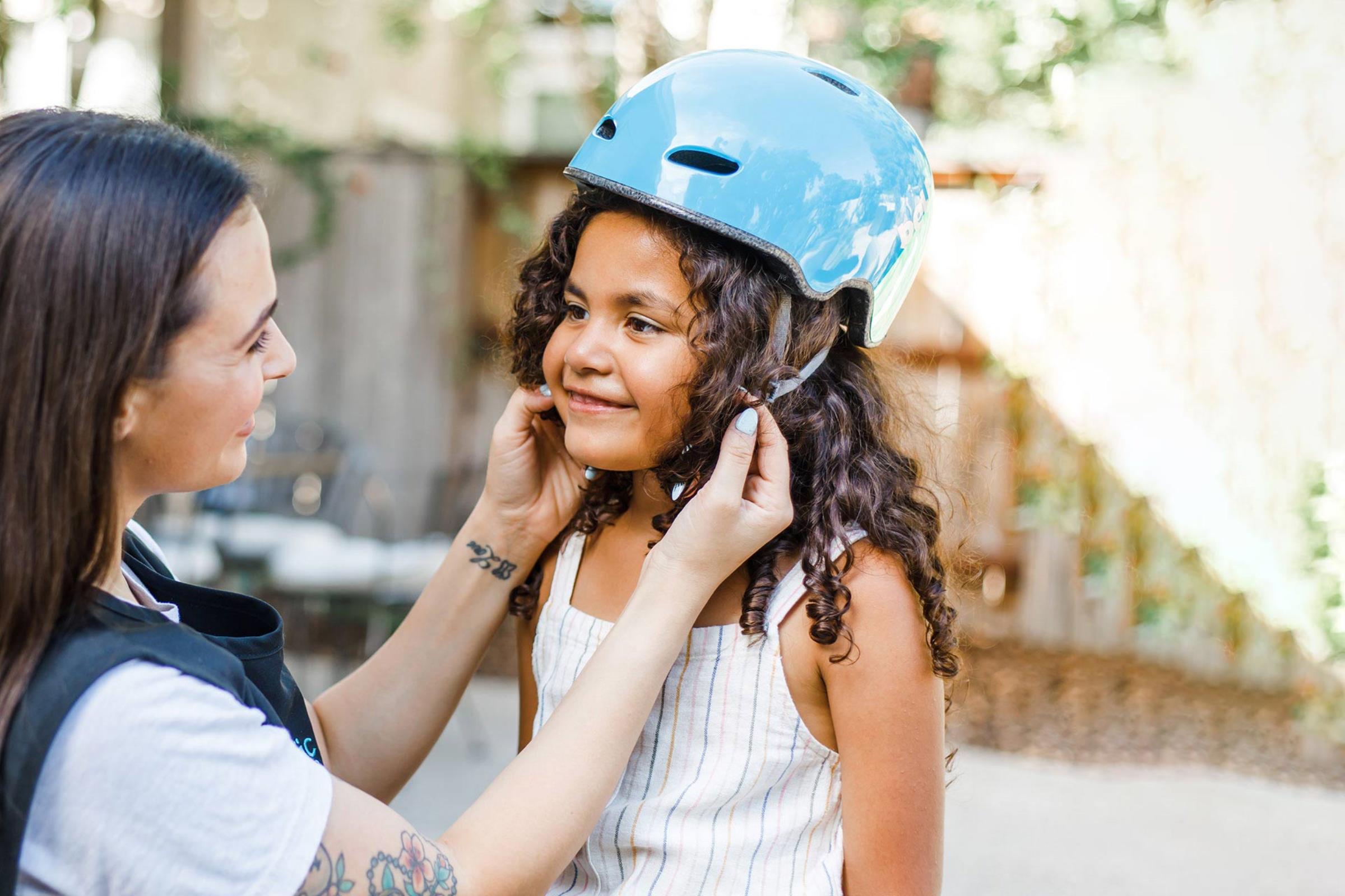 Female care provider putting bicycle helmet on female child